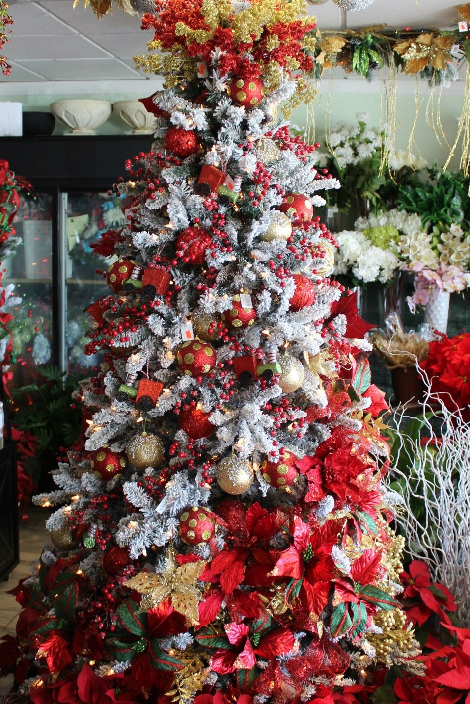 Árbol de Navidad nevado con pascuas rojas y esferas doradas, montado en la tienda de Bella Flor