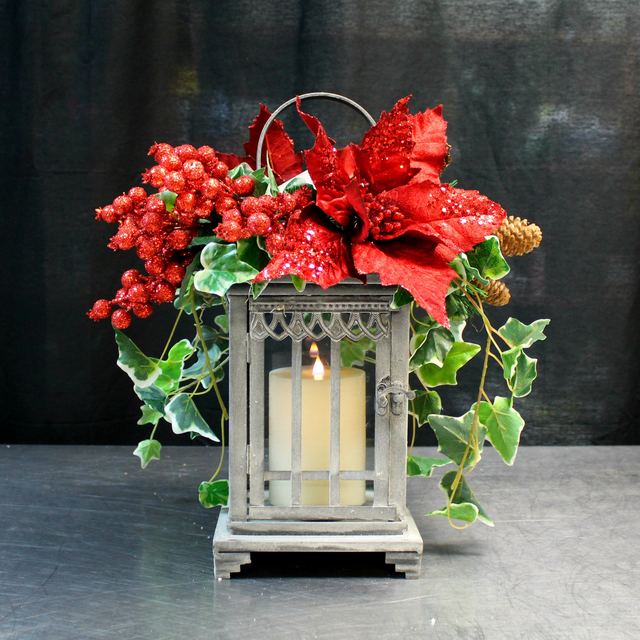 Farol de cristal con vela encendida, pascua roja y hiedra